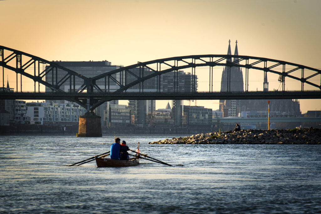 Köln am Rhein mit Blick auf die Eisenbahnbrücke, Kranhäuser, Dom, auf dem Rhein ist ein Paddelboot
